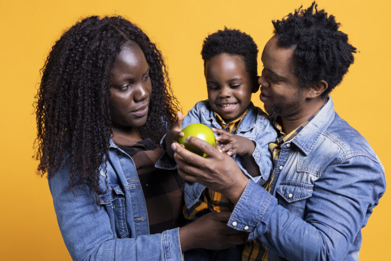 Adorable small child looking at an apple against yellow background