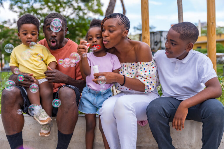 African black ethnic family with children in playground having fun blowing soap bubbles