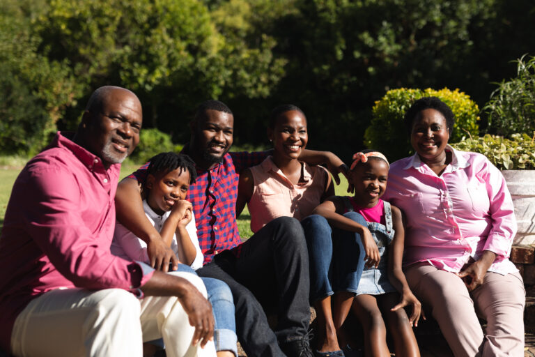 Smiling african american parents with children and their grandparents sitting embracing outdoors. three generation family spending time together